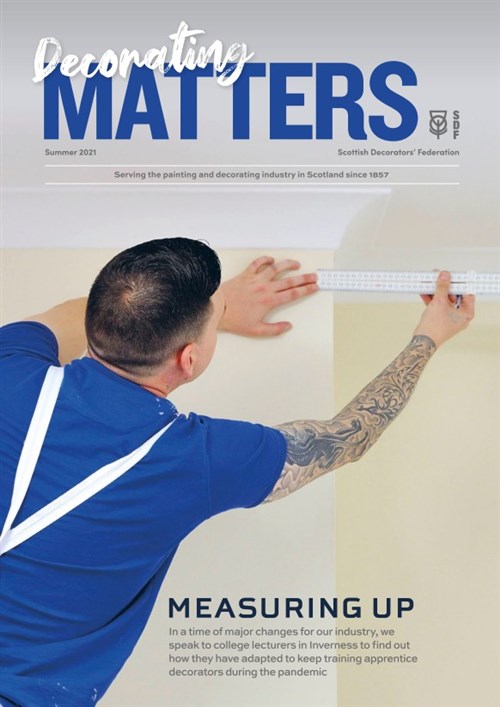 Cover, Decorating Matters - Summer 2021. A tattooed decorator in a blue tshirt measures a wall with a ruler